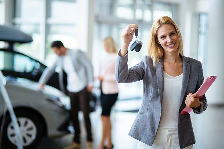 Motor trade salesperson holding keys up with a smile in a car showroom