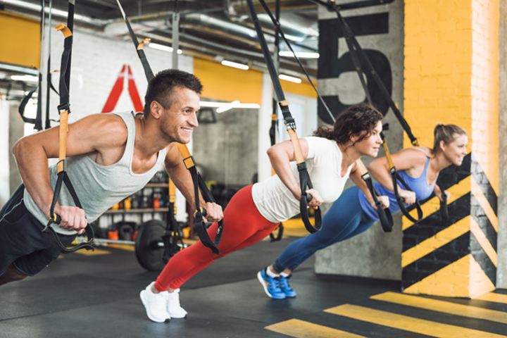 Three people working out in a gym using sports fitness equipment