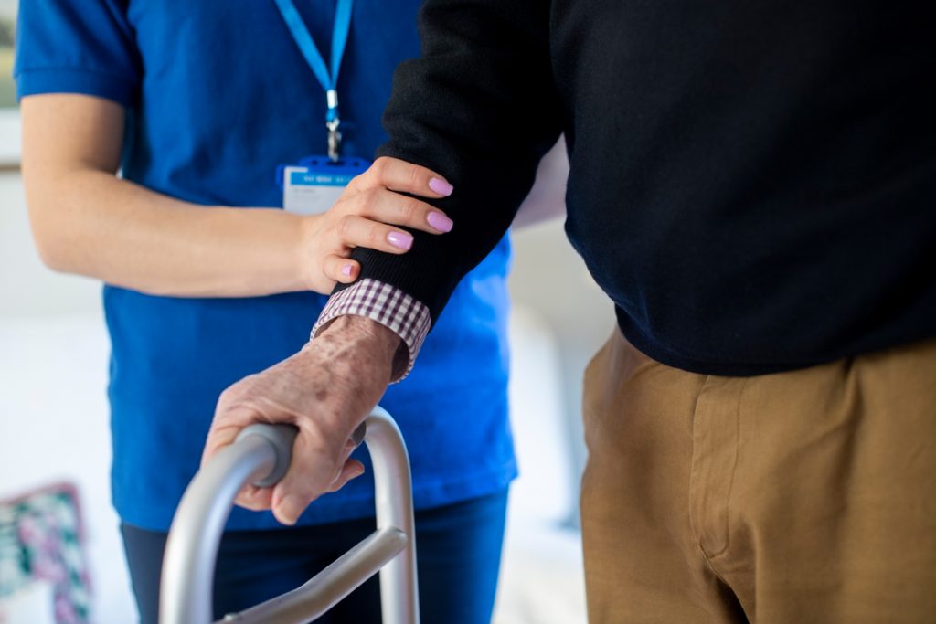 Senior Man With Hands On Walking Frame With Care Worker