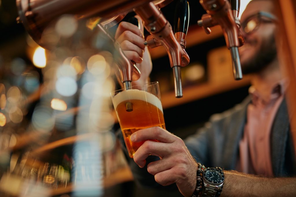 barman pouring beer while standing in pub