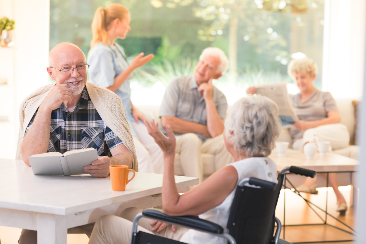 Elderly man talking with disabled woman while sitting together at table in common room