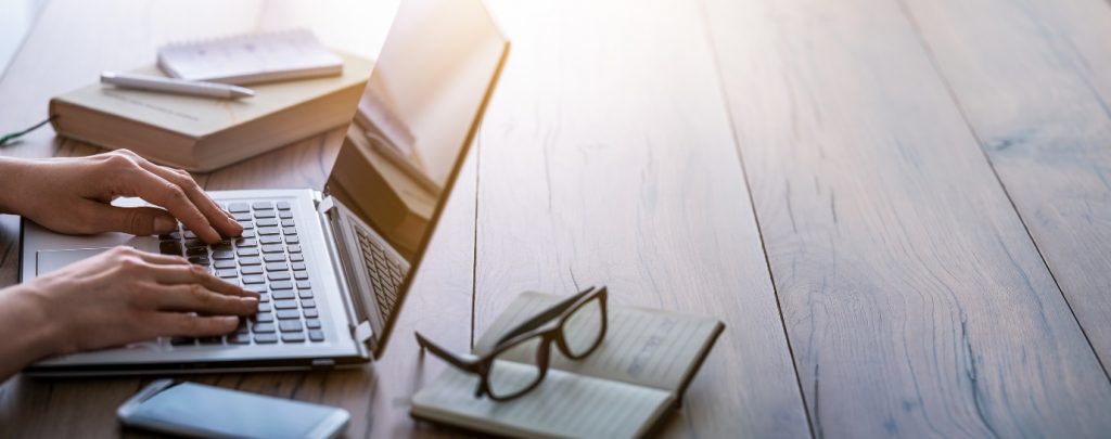 hands working on laptop with books and glasses on background