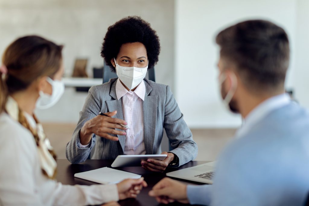 manager with face mask using touchpad while talking to her clients on a meeting in the office