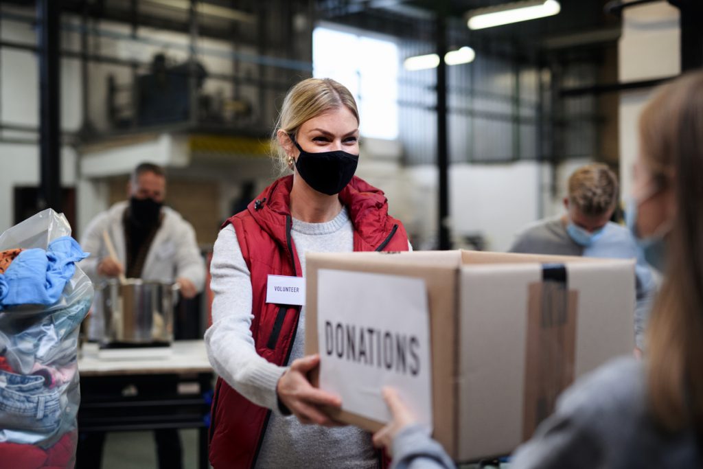 Volunteers working with food and clothes in community charity donations center, coronavirus concept.