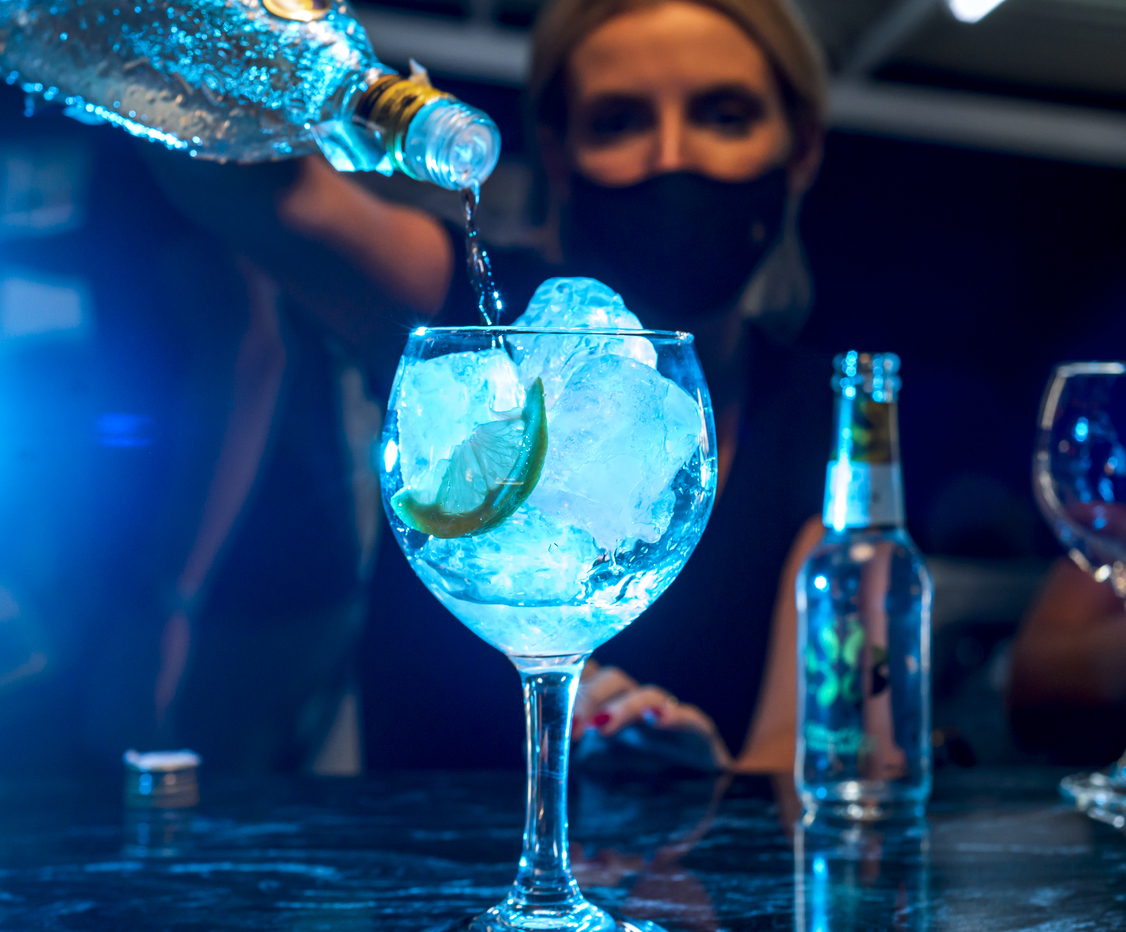 Young waitress with protective mask prepares a gin and tonic cocktail in a nightclub.