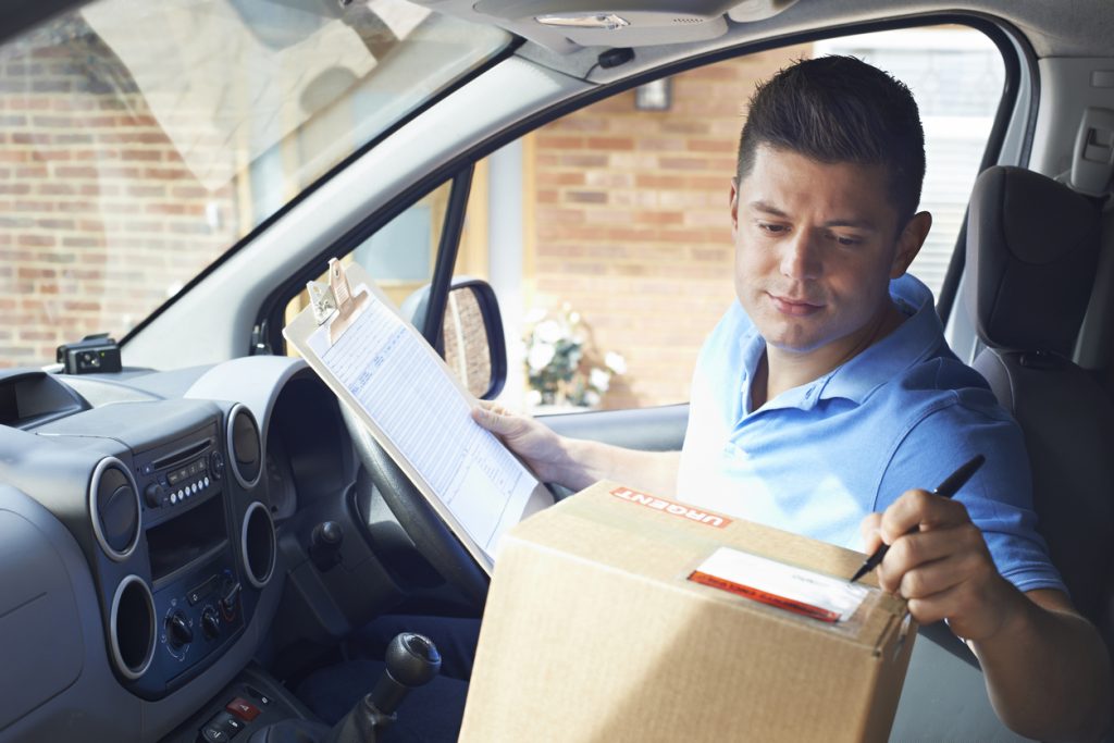 Courier In Van With Clipboard Delivering Package To Domestic House