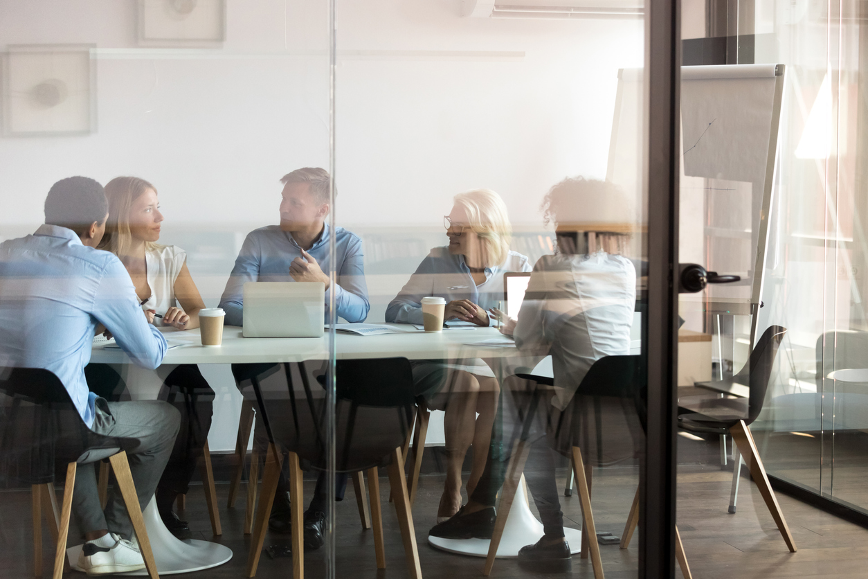 Office workers at modern office boardroom behind closed doors, view through the glass wall. Diverse staff led by ceo discussing  cybersecurity and more