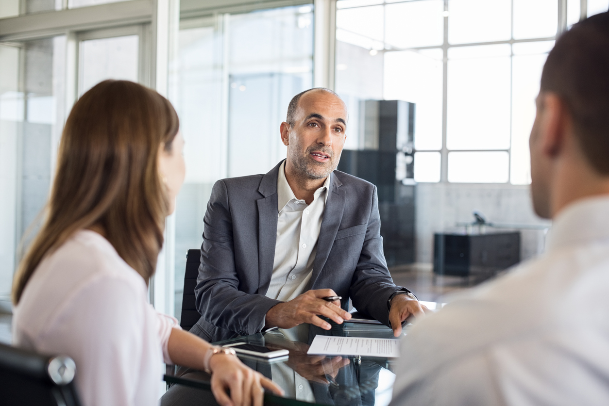 Mature insurance broker showing new policy to young couple. Happy advisor discussing with a couple their insurance contracts