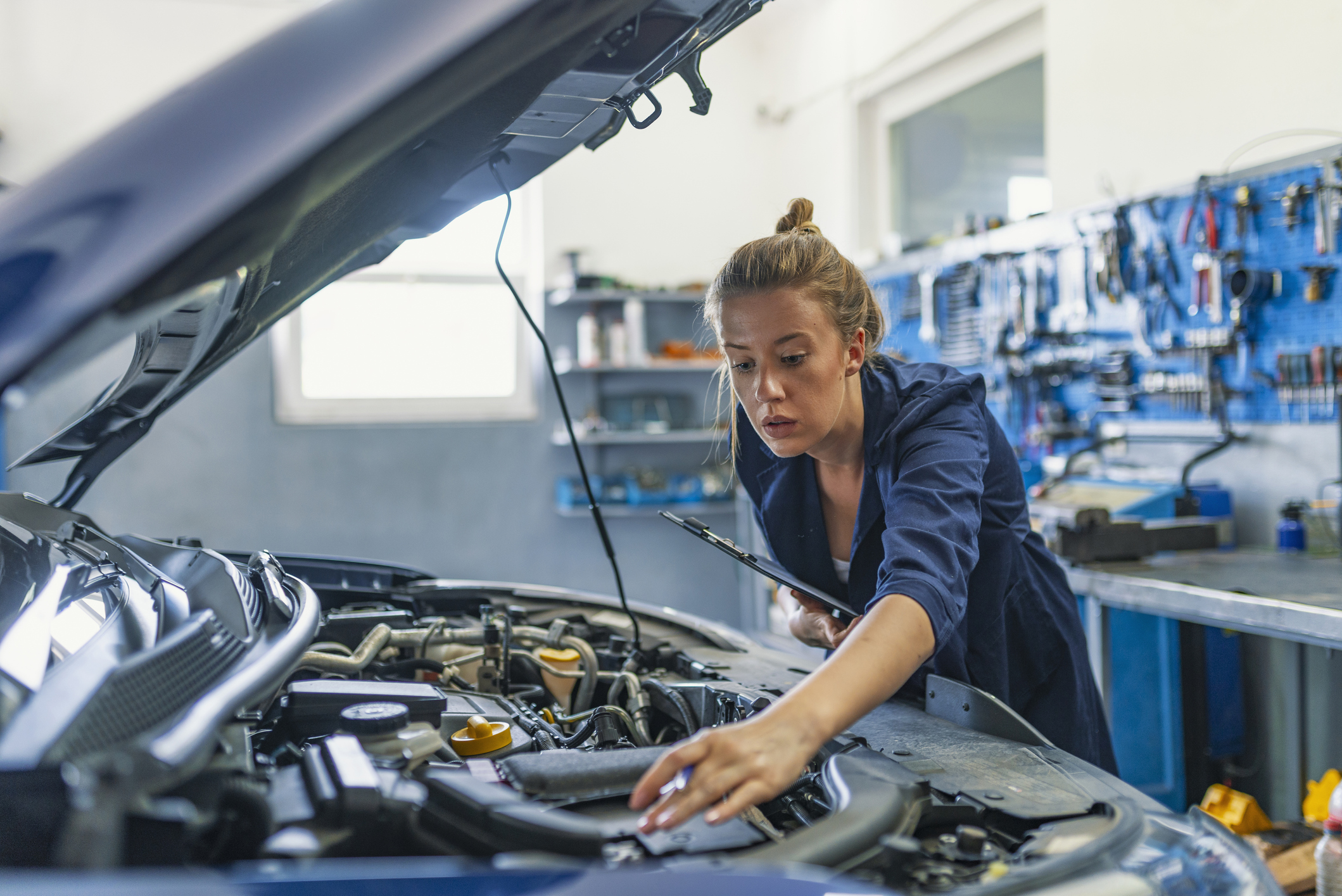 Mechanic working under the hood at the repair garage. Portrait of a happy mechanic woman working on a car in an auto repair shop. Female mechanic working on car